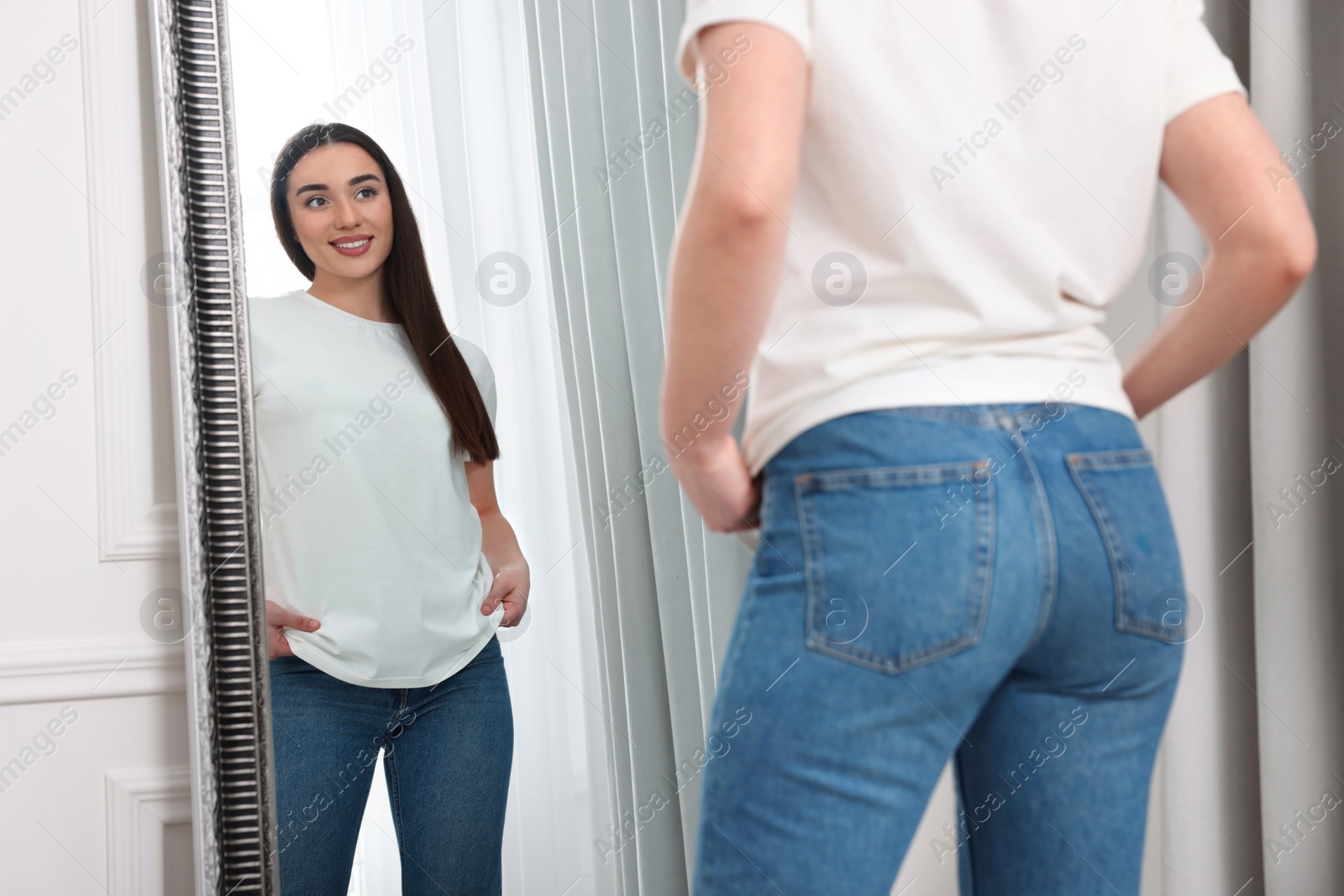 Photo of Young woman in stylish jeans near mirror indoors