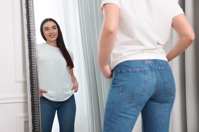 Young woman in stylish jeans near mirror indoors