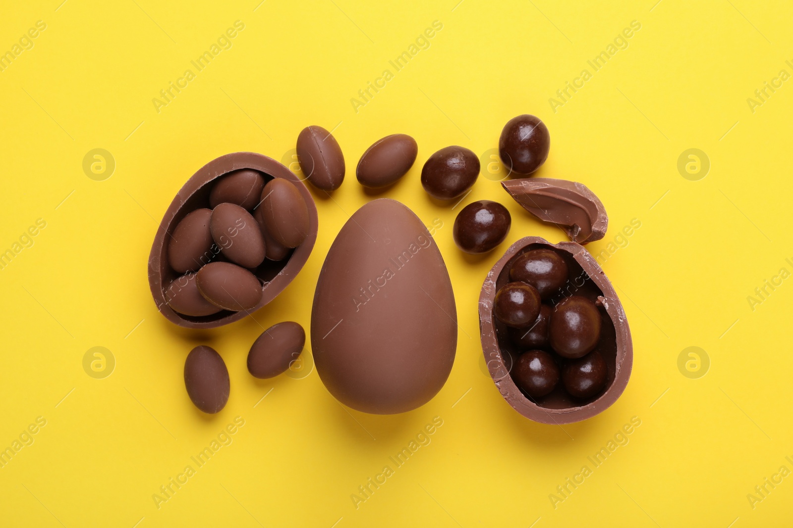 Delicious chocolate eggs and sweets on yellow background, flat lay Photo of Delicious chocolate eggs and sweets on yellow background, flat lay
