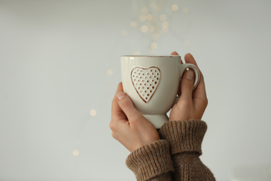 Photo of Woman holding cup of delicious morning coffee against light grey background, closeup