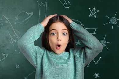 Image of Emotional little girl near chalkboard with different drawings