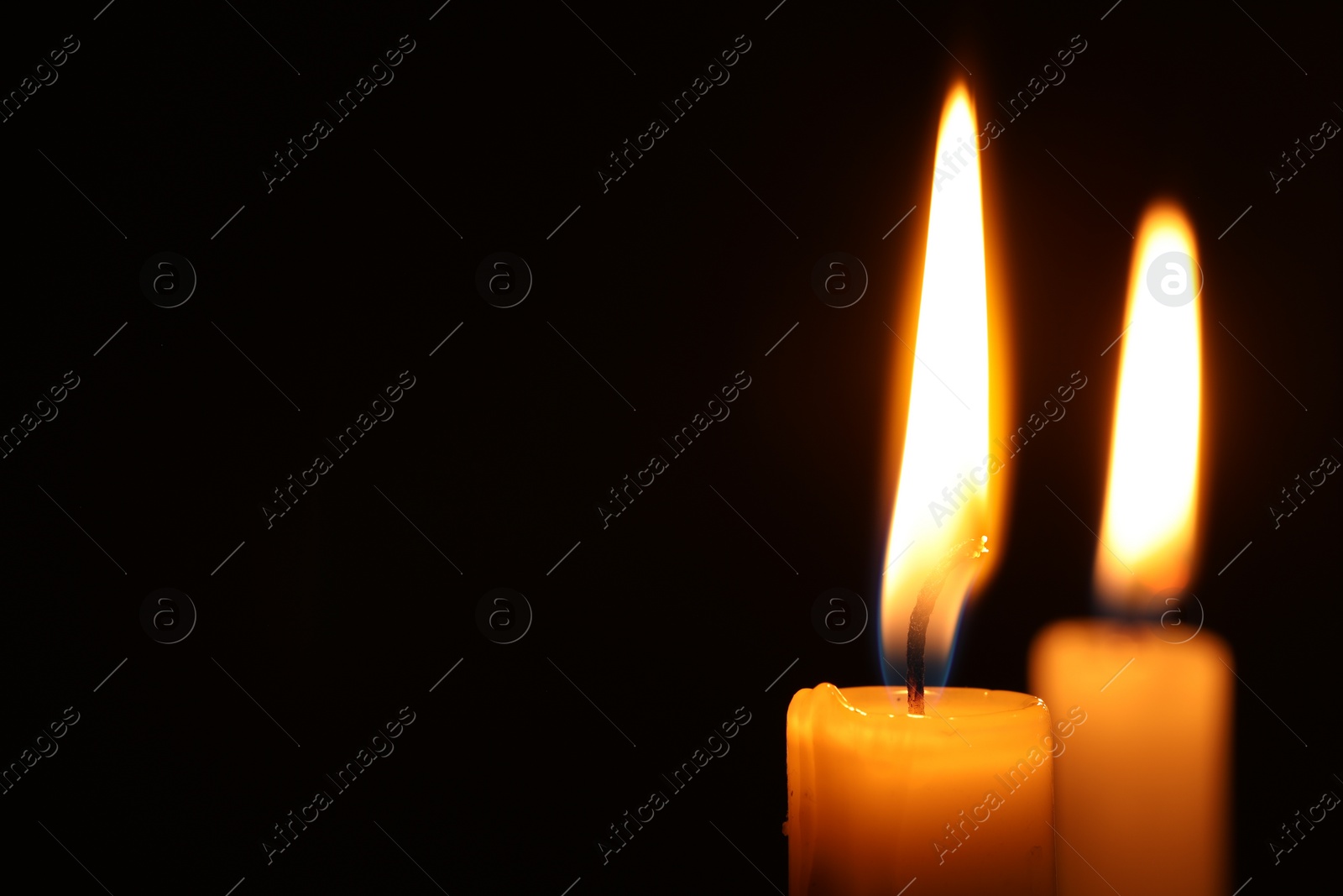 Photo of Burning candles on black background, closeup. Space for text