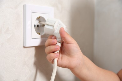 Photo of Little child playing with electrical socket and plug indoors, closeup. Dangerous situation