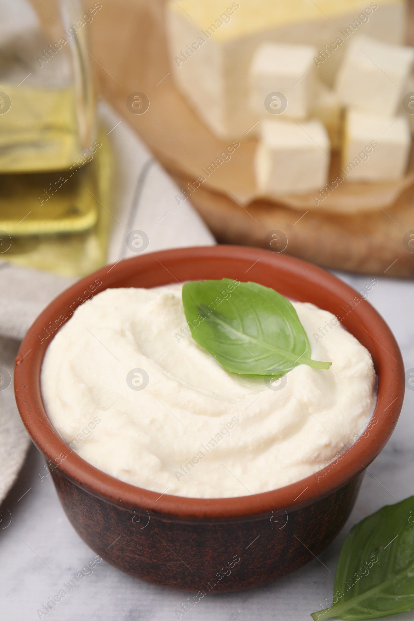 Photo of Delicious tofu sauce and basil leaves on white table, closeup