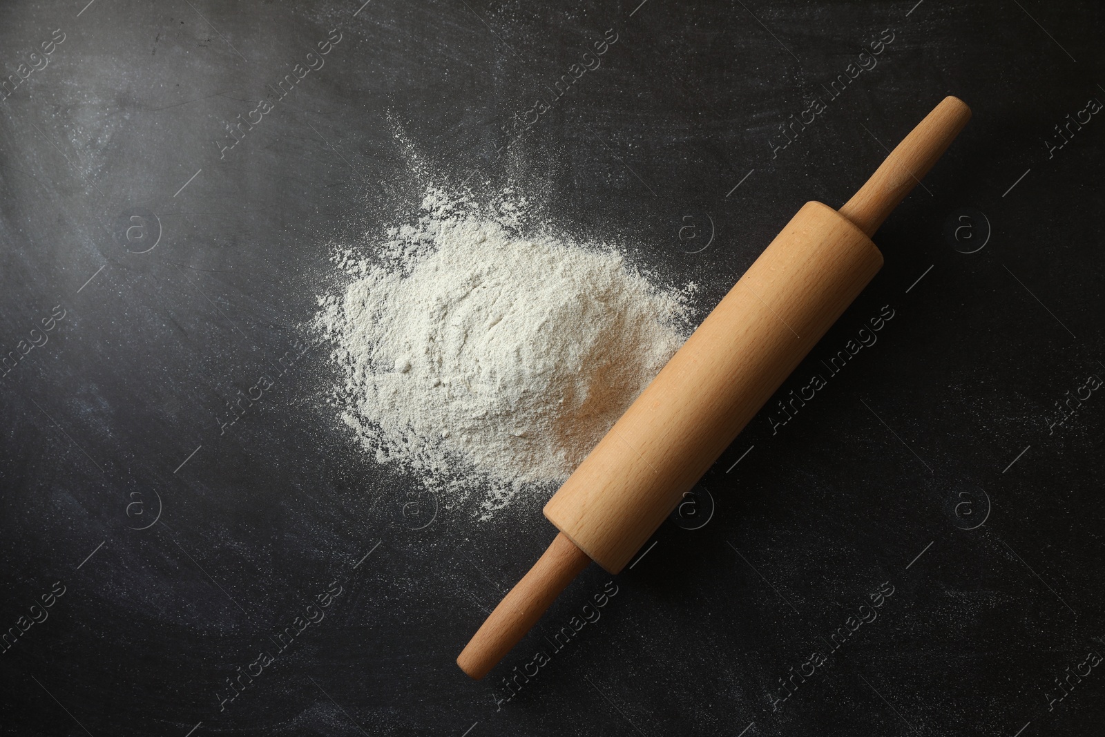 Photo of Flour and rolling pin on black table, top view