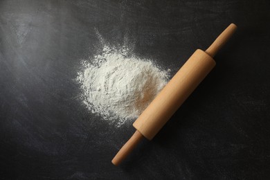 Photo of Flour and rolling pin on black table, top view