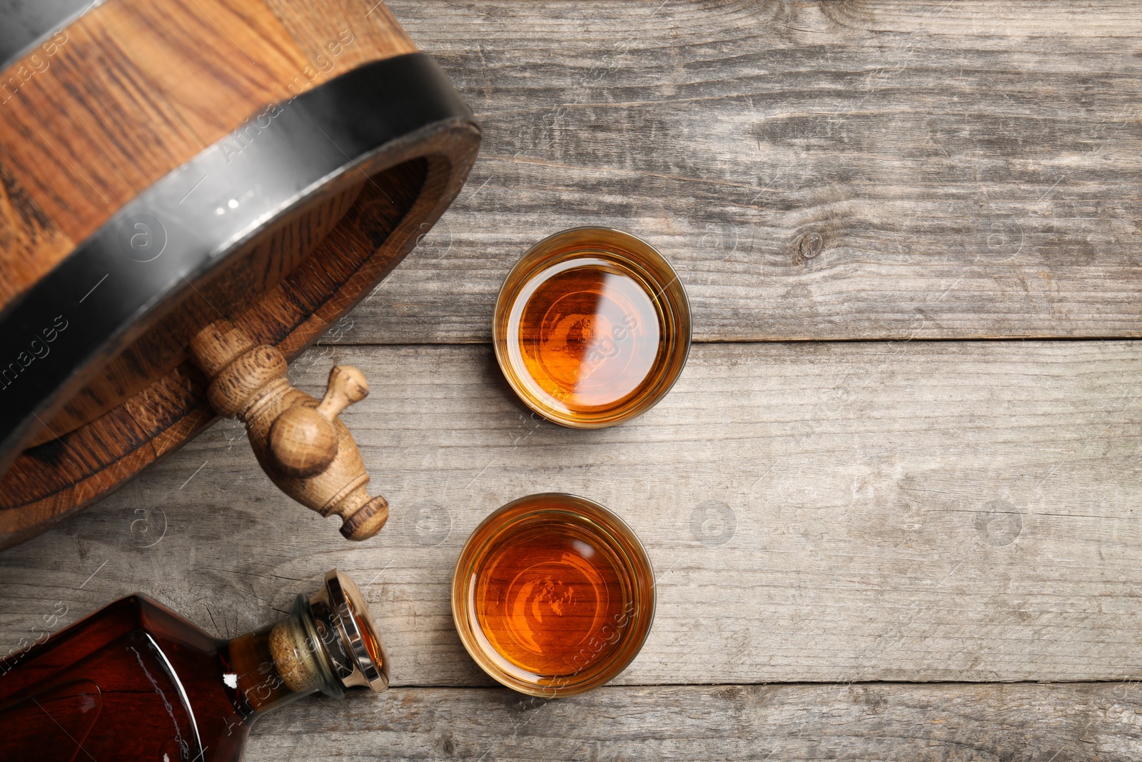 Photo of Glasses and bottle of whiskey with wooden barrel on table, flat lay. Space for text