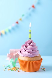 Photo of Birthday cupcake with burning candle and gift box on light blue table