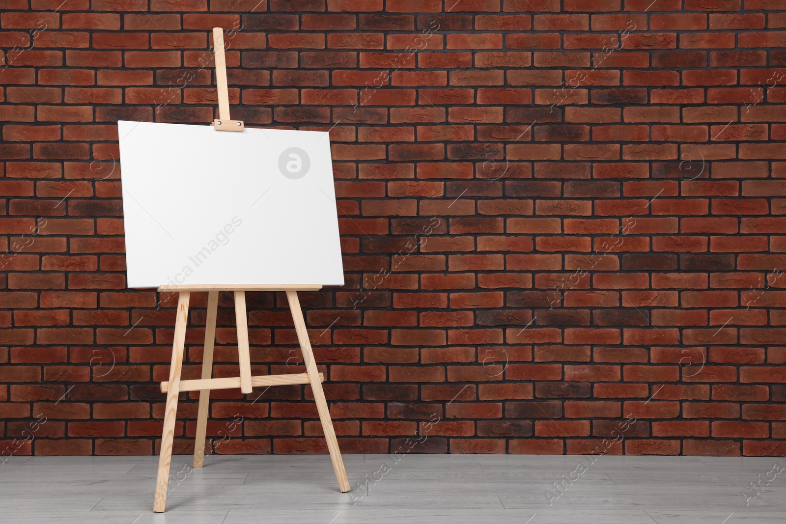 Photo of Wooden easel with blank canvas near brick wall indoors. Space for text