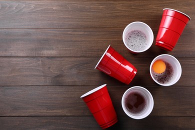 Photo of Plastic cups and ball on wooden table, flat lay with space for text. Beer pong game
