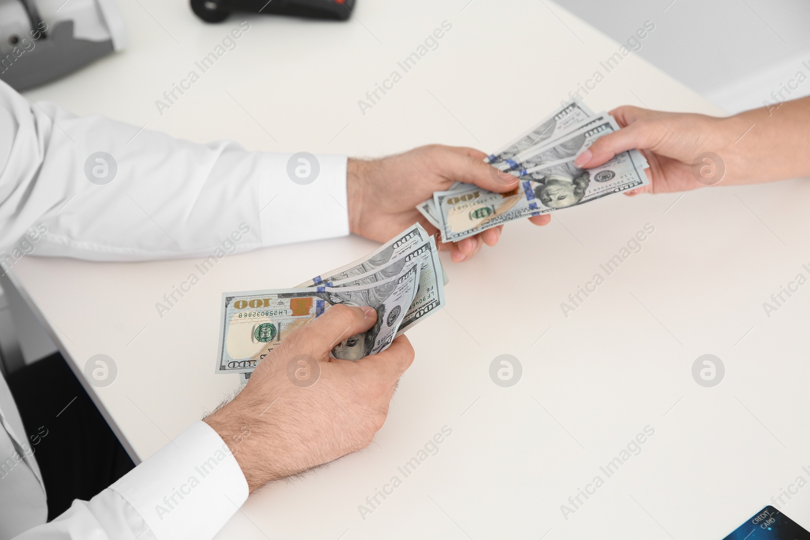 Photo of Male teller giving money to woman at table, closeup