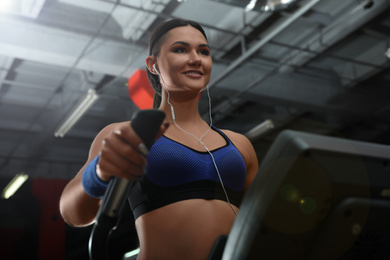 Young woman working out on elliptical trainer in modern gym, low angle view