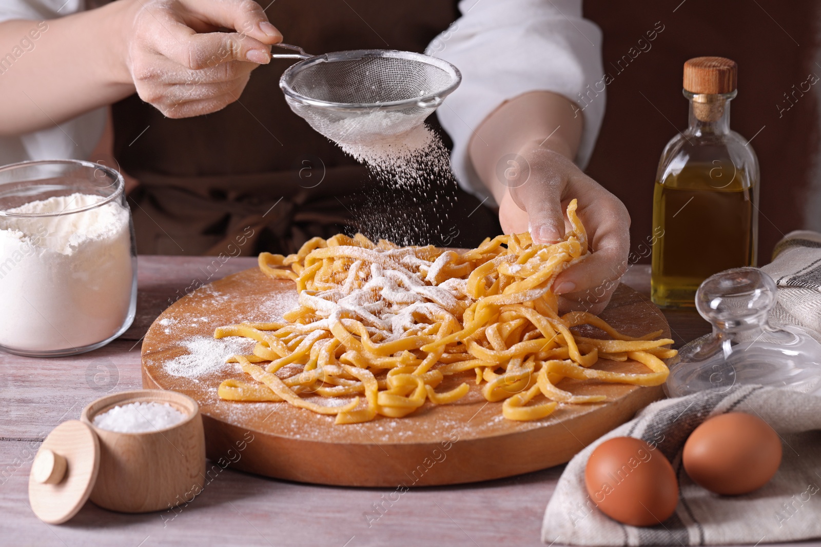 Photo of Making homemade pasta. Woman powdering noodles with flour at wooden table, closeup