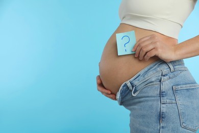 Pregnant woman with sticky note on light blue background, closeup. Choosing baby name