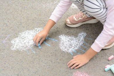 Photo of Little child drawing white clouds with chalk on asphalt, closeup
