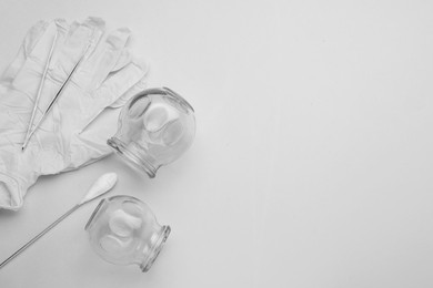 Photo of Glass cups, torch, gloves and tweezers on light grey background, flat lay with space for text. Cupping therapy