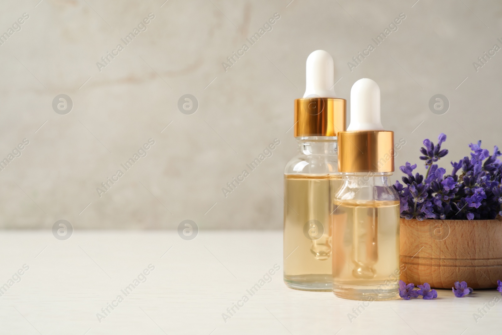 Photo of Bottles of essential oil and lavender flowers on white wooden table. Space for text