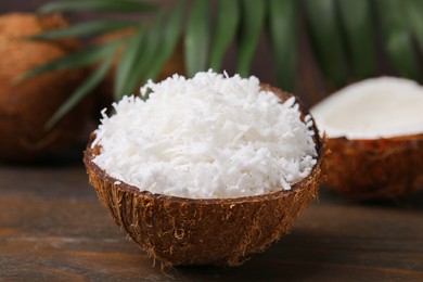 Coconut flakes in nut shell on wooden table, closeup