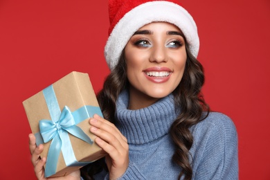 Beautiful woman in Santa hat with Christmas gift on red background