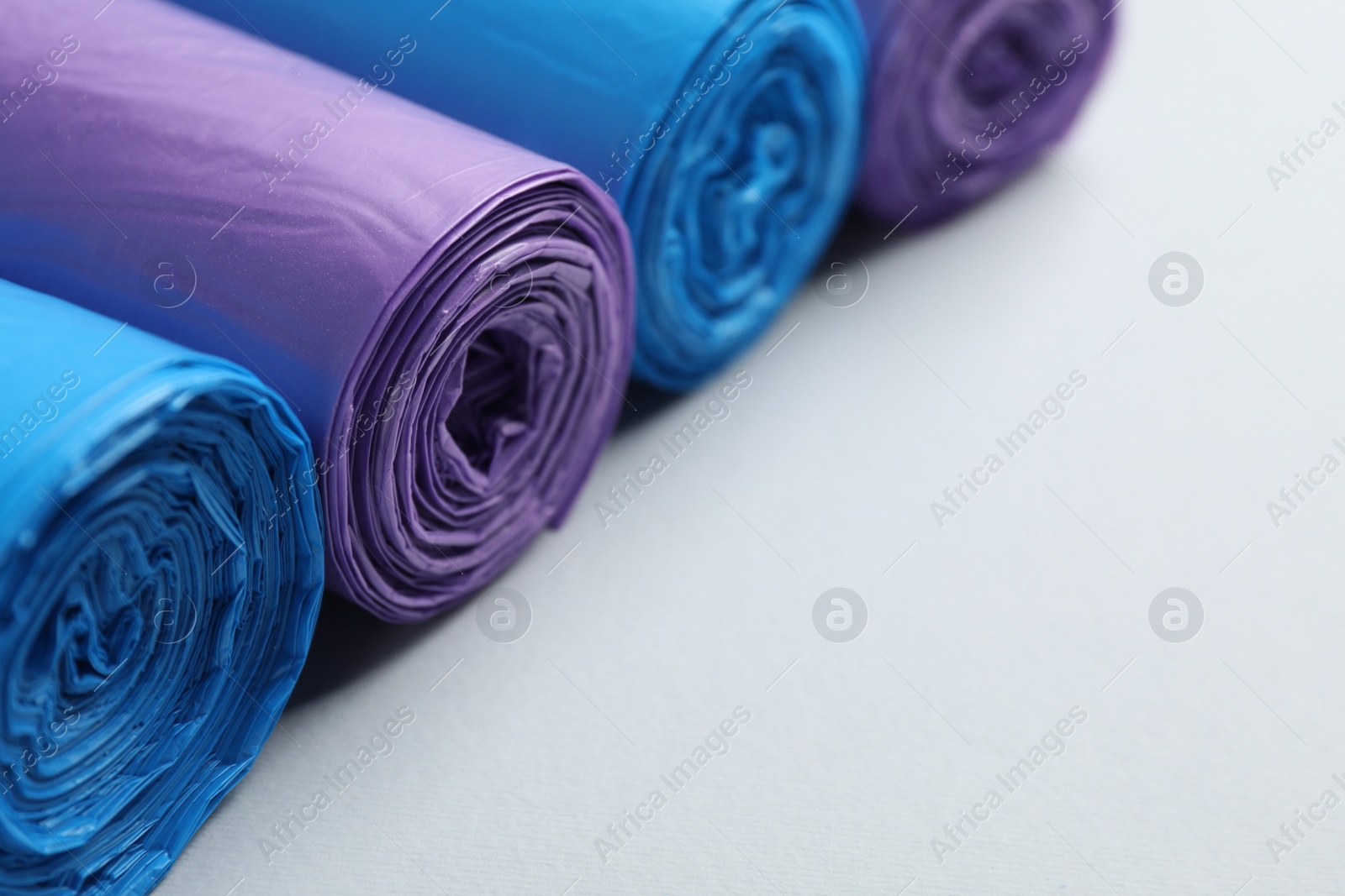 Photo of Rolls of different color garbage bags on light background, closeup. Space for text