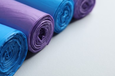 Rolls of different color garbage bags on light background, closeup. Space for text