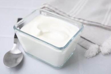 Photo of Delicious natural yogurt in glass bowl and spoon on white table, closeup