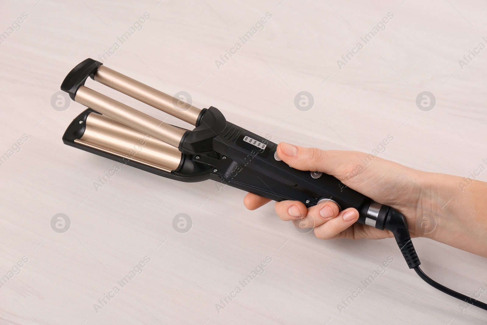 Photo of Woman holding modern triple curling iron on wooden background, closeup