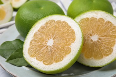 Photo of Whole and cut sweetie fruits with green leaves on plate, closeup