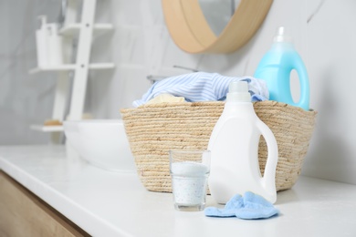 Photo of Bottles of detergent and children's clothes on countertop in bathroom