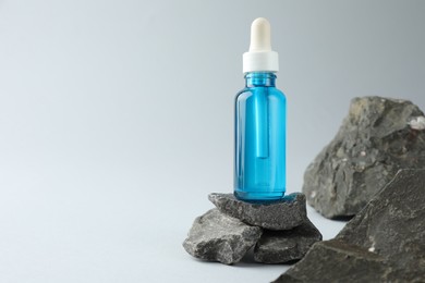 Photo of Bottle of cosmetic serum on stones against light grey background, space for text