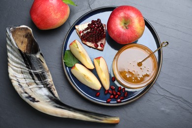 Honey, pomegranate, apples and shofar on black table, flat lay. Rosh Hashana holiday
