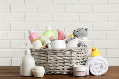 Photo of Wicker basket with different baby cosmetic products, accessories and toys on wooden table