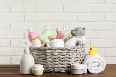 Wicker basket with different baby cosmetic products, accessories and toys on wooden table