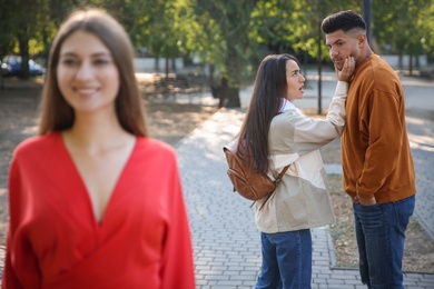 Photo of Disloyal man looking at another woman while walking with his girlfriend in park