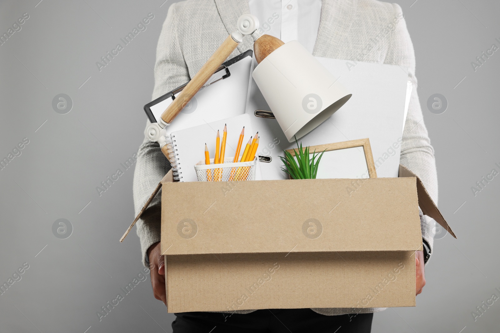 Photo of Unemployed man with box of personal office belongings on light grey background, closeup