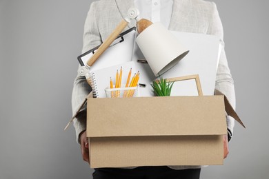 Unemployed man with box of personal office belongings on light grey background, closeup