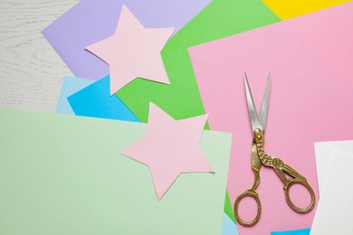 Pair of scissors with colorful paper sheets on white wooden table, flat lay. Space for text