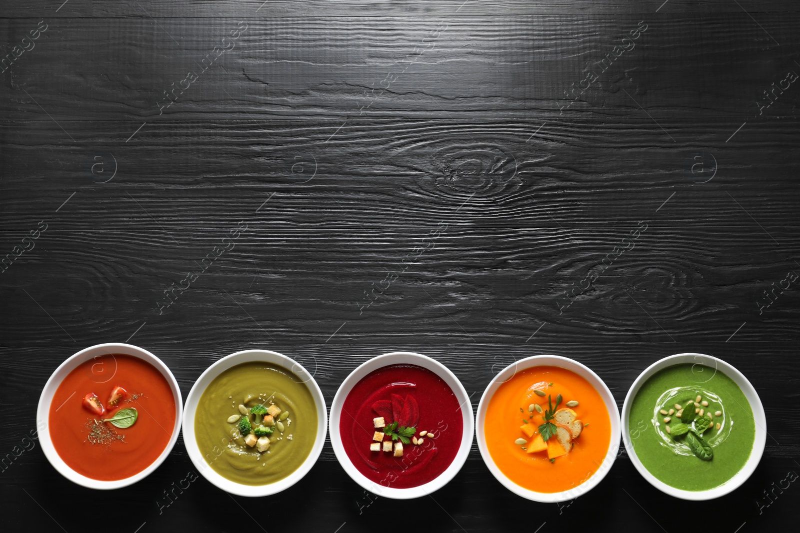 Photo of Various soups in bowls and space for text on wooden background, top view. Healthy food