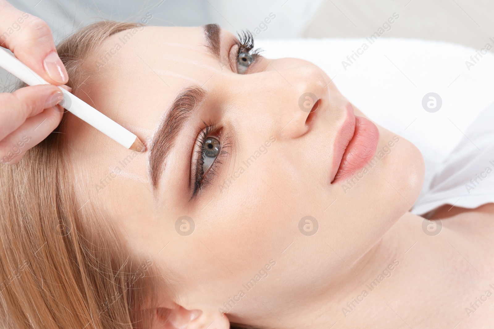 Photo of Cosmetologist preparing young woman for  eyebrow permanent makeup procedure, closeup