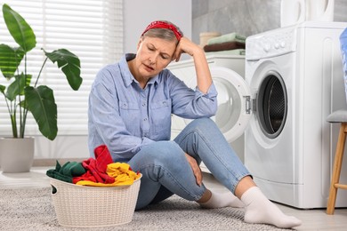 Sad housewife with laundry near washing machine at home