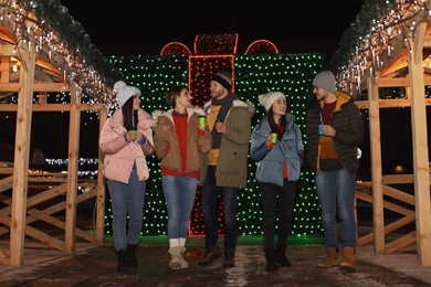 Photo of Happy friends with cups of mulled wine at winter fair