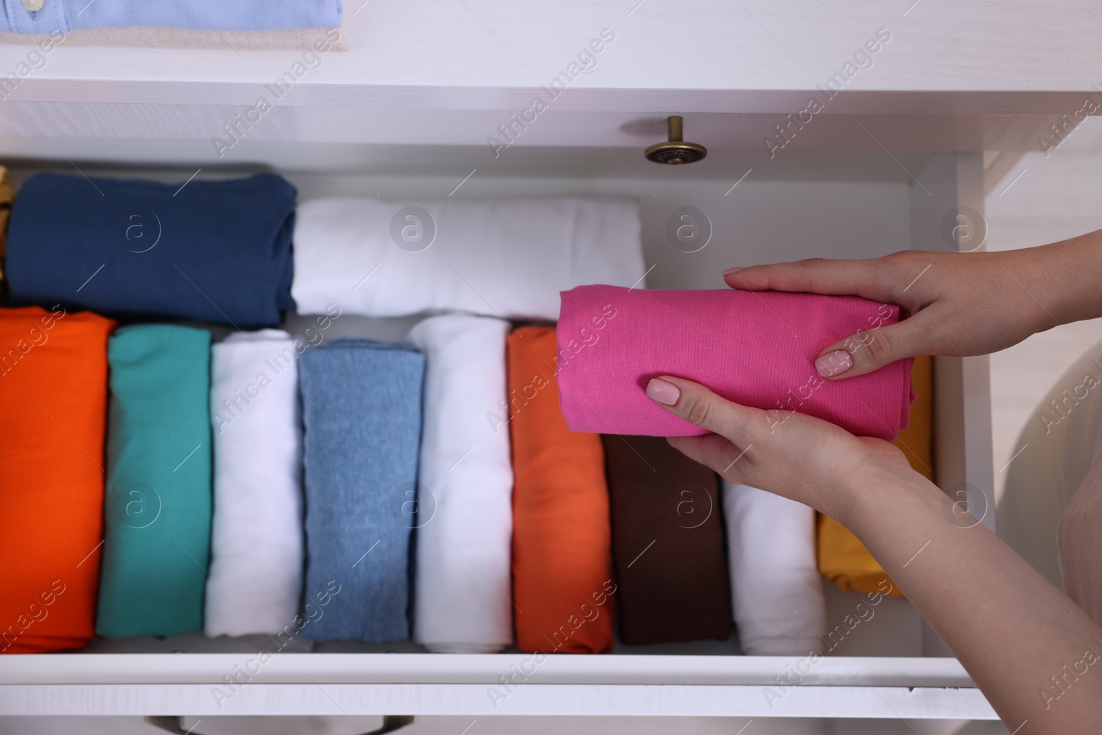 Photo of Woman putting rolled shirt into drawer, top view. Organizing clothes