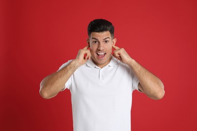 Excited man covering ears with fingers on red background