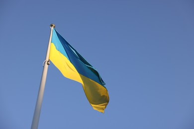 Flag of Ukraine fluttering against blue sky, low angle view. Space for text