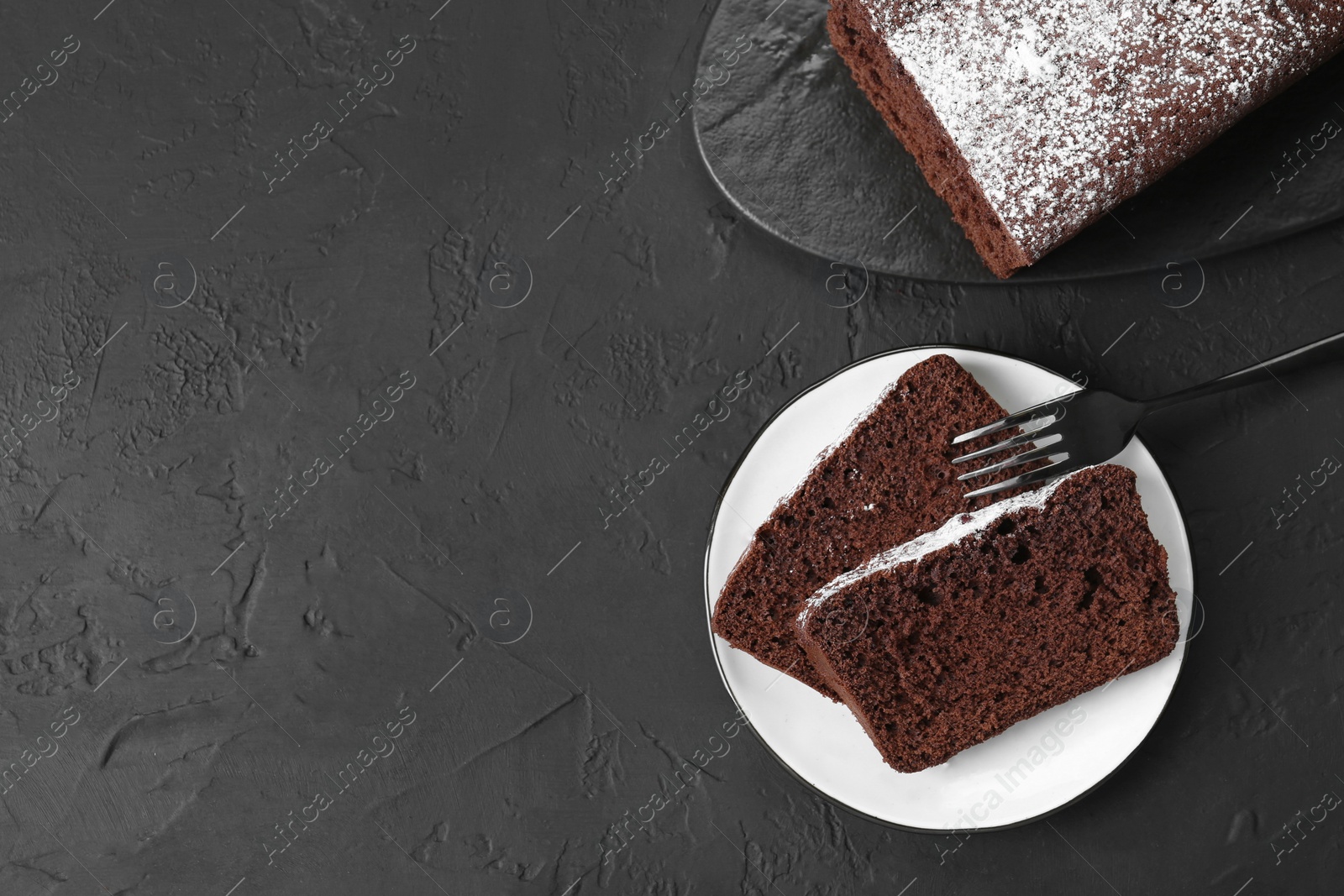 Photo of Tasty chocolate sponge cake with powdered sugar on black textured table, flat lay. Space for text