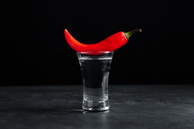 Red hot chili pepper and vodka in shot glass on grey table against black background