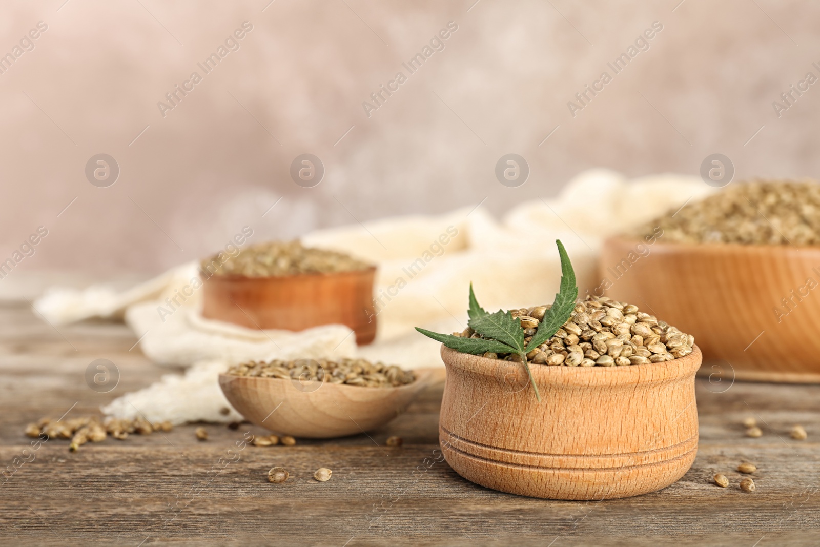 Photo of Bowl of hemp seeds on wooden table against color background