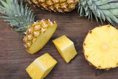 Photo of Cut and whole ripe pineapples on wooden table, flat lay