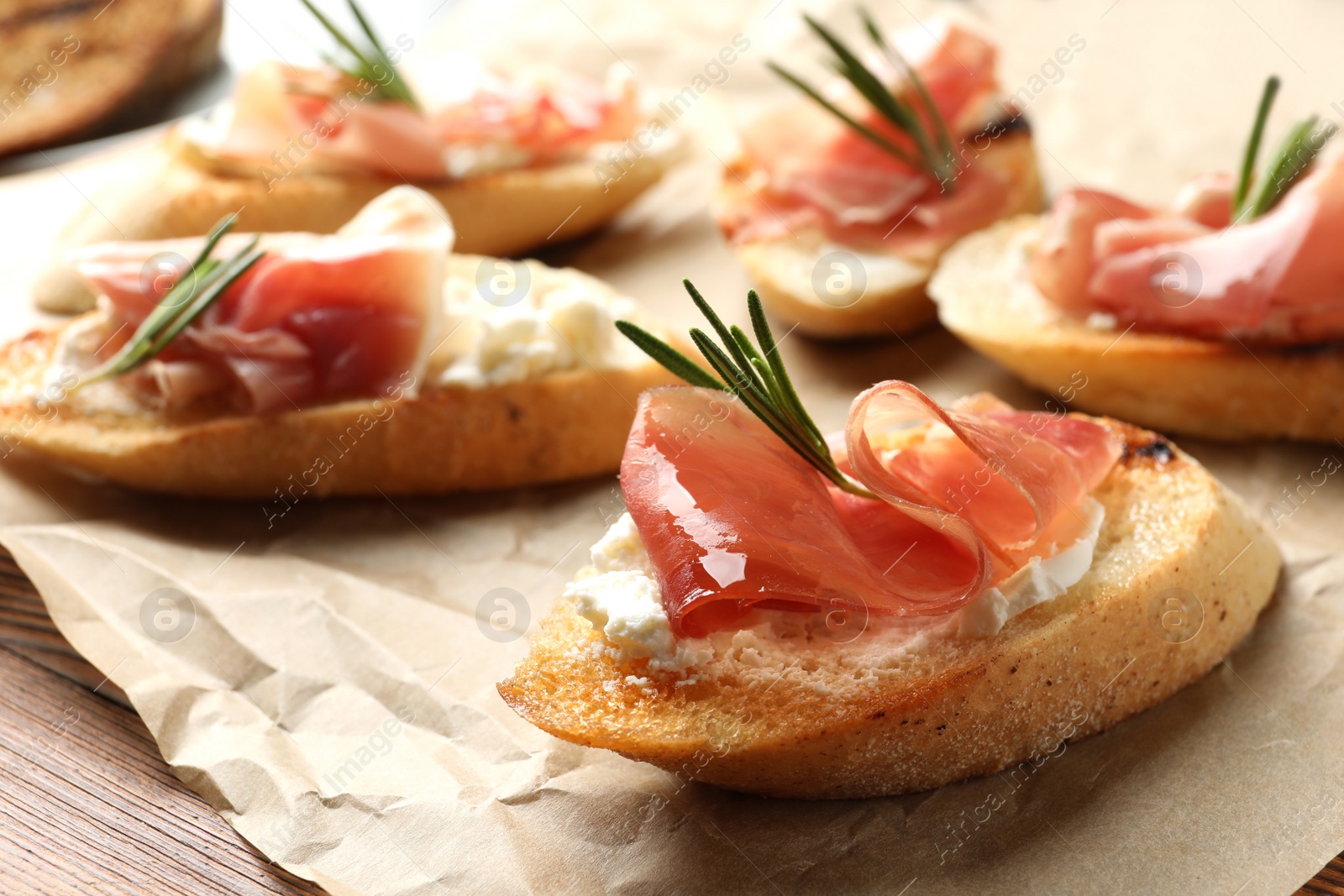 Photo of Tasty bruschettas with prosciutto and cream cheese on parchment, closeup