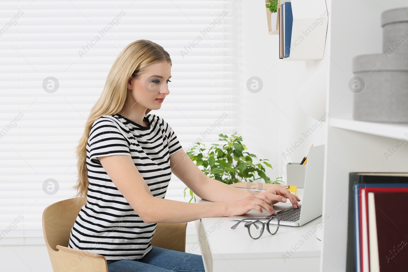 Photo of Home workplace. Woman working on laptop at white desk in room